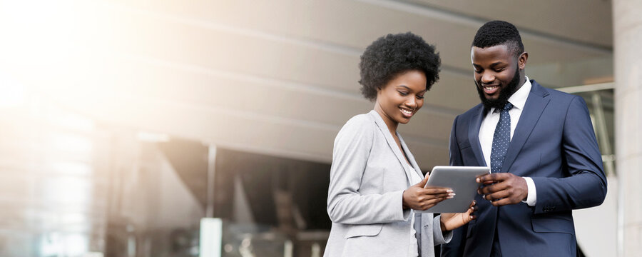 Dark-skinned business people using digital tablet and discussing new project details outdoors
