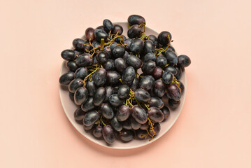 Plate with sweet black grapes on pink background