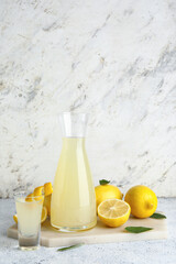 Board with bottle and shot of tasty Limoncello on white background