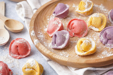 Wooden plate with colorful raw dumplings and flour on white background