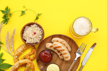 Plate with tasty Bavarian sausages, sauces, sauerkraut, pretzels and mug of beer on yellow background. Oktoberfest celebration