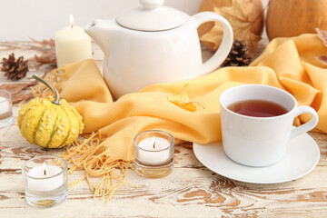 Burning candles with cup of tea, scarf, pumpkin and autumn leaf on table