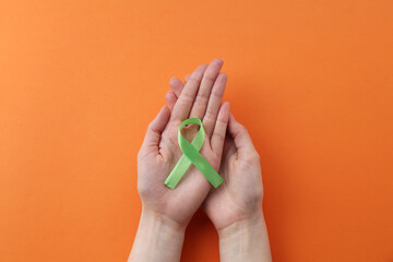 Woman with light green awareness ribbon on orange background, top view