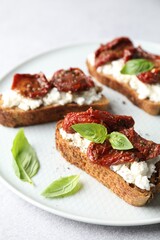 Delicious ricotta bruschettas with sun dried tomatoes and basil on light table, closeup