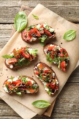 Delicious ricotta bruschettas with tomatoes, arugula and basil on wooden table, top view