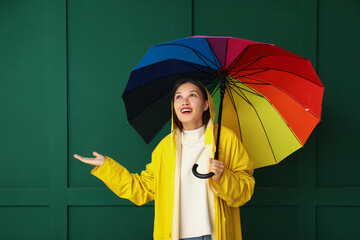 Beautiful young Asian woman in raincoat with umbrella on green background