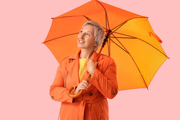 Beautiful mature woman with umbrella on pink background