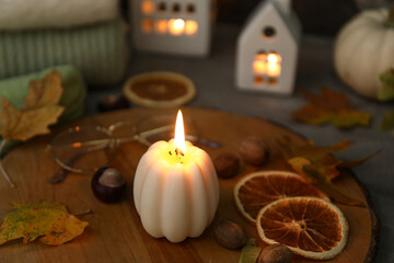 Wooden board with burning candle and autumn decor on table, closeup