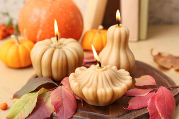 Beautiful composition with burning candles in shape of pumpkin and autumn leaves on beige background