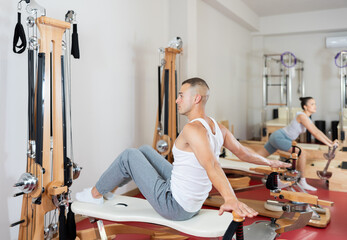 Active young guy training her back and shoulders turning handles of exercise machine in fitness hall