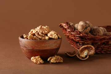 Bowl and wicker basket of tasty walnuts on brown background