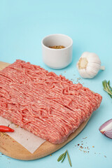 Wooden board of fresh minced meat with spices on blue background