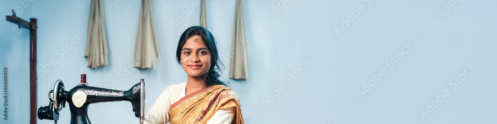 Wall mural Woman working in a sewing workshop making clothes in Asia. Panoramic image with large copy space.