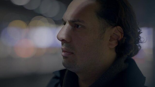 A man looking through a window in a modern urban setting at night, with a serious expression