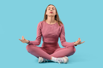 Beautiful young woman in sportswear meditating on blue background