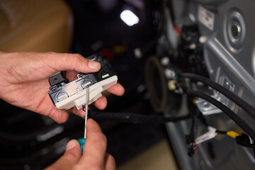 A mechanics hands are seen repairing the cars interior door panel controller inside the vehicle