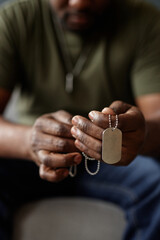 Vertical close up of unrecognizable Black man as army veteran holding dog tags in hands during...