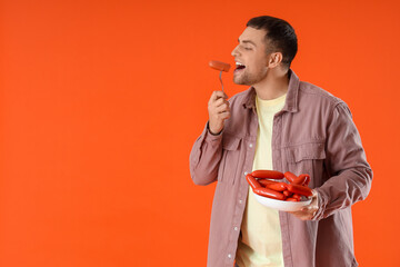 Fototapeta premium Young man with plate of tasty sausages on orange background