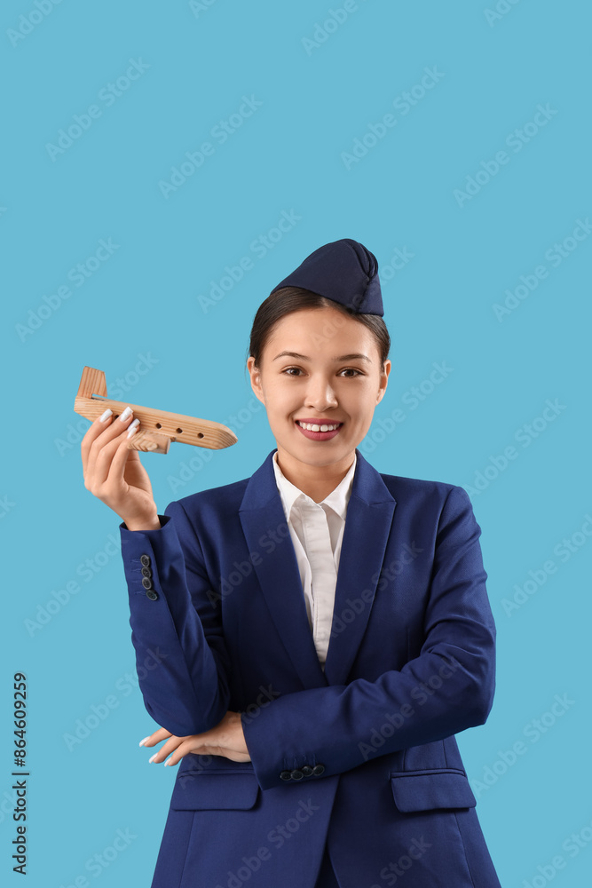 Sticker Young Asian stewardess with wooden airplane on blue background