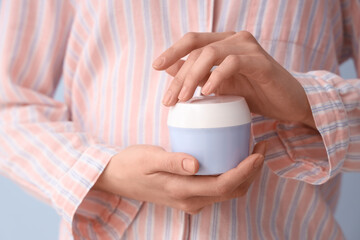 Woman in stylish pajamas holding jar of cream on color background, closeup