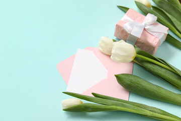 Envelope with blank card, gift box and white tulips on turquoise background