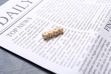 Daily newspaper and word NEWS made of cubes on blue wooden background