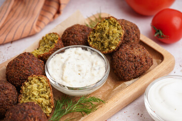 Wooden board with delicious falafel balls and sauce on light background, closeup
