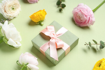Gift box with beautiful ranunculus flowers and eucalyptus on green background