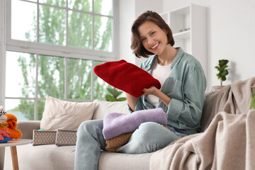 Young woman folding different clothes and sitting on sofa at home