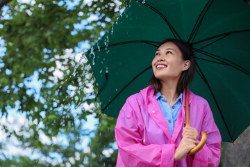 Portrait of young Asian woman man in raincoat holding umbrella outdoors on rainy day