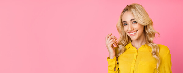 A young woman with blonde hair and a bright smile is pictured against a pink backdrop. She is wearing a yellow shirt and has her hand resting on her cheek, panorama with copy space
