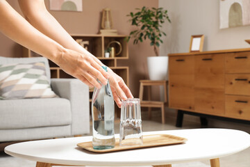 Woman with bottle of water and glass on table at home, closeup