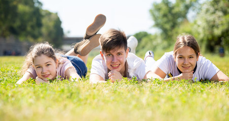 Fototapeta premium Cheerful teen friends gaily spending time outdoors in summertime, lying together on green lawn