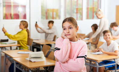 Portrait of unhappy kid girl studying in classroom at secondary school, learning lessons