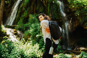 One young caucasian woman is taking a break from hiking near the river and waterfall in the forest	