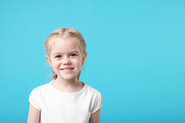 Portrait of cute little girl on light blue background, space for text