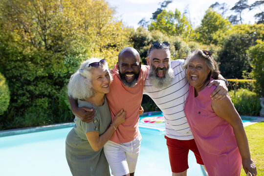 Diverse group of senior friends hugging and smiling by swimming pool outdoors