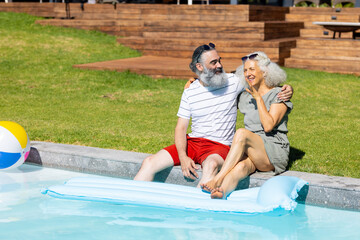 Senior couple sitting by pool, relaxing and enjoying sunny day together