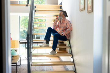 Sitting on stairs, senior man drinking coffee and looking out window at home