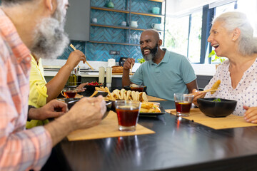 At home, Diverse group of senior friends enjoying meal and laughing together in kitchen