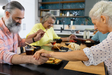 At home, Group of senior friends holding hands and praying before meal in kitchen