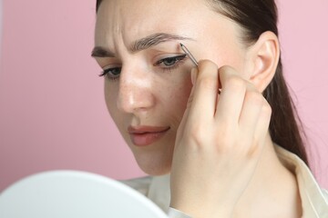 Young woman plucking eyebrow with tweezers on pink background, closeup