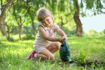 Fototapeta premium Cute little girl watering tree in garden
