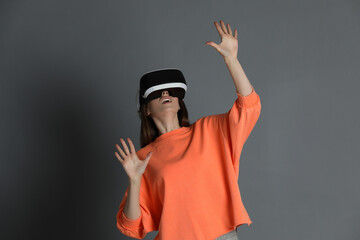 Surprised woman using virtual reality headset on gray background