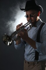 Professional musician playing trumpet on dark background with smoke