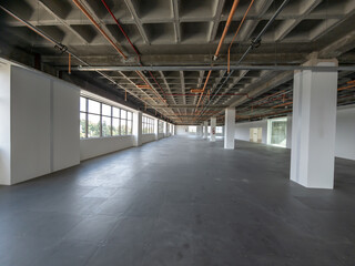 A large, empty office building interior with plenty of windows and exposed industrial pipes on the ceiling.