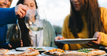 Close-up Happy friends eating pizza and drink wine outside restaurant terrace. Group of people...