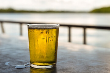 light gold beer lager in a transparent glass stands on a table on a blurred background of the river
