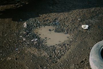 Water-filled pothole on a damaged road, highlighting issues with infrastructure and maintenance.