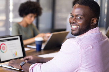 Smiling, African American businessman using laptop with charts in casual office setting